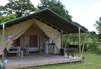 Tenda safari al Camping Domaine Bleu Celeste in Francia con veranda, arredi rustici e vista sulla natura.