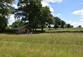 Tente safari au Camping Domaine Bleu Celeste en France, entourée de prairies, fleurs et arbres verdoyants.