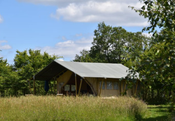 Safari-Zelt auf dem Campingplatz Domaine Bleu Celeste in Frankreich, umgeben von Bäumen und hohem Gras.