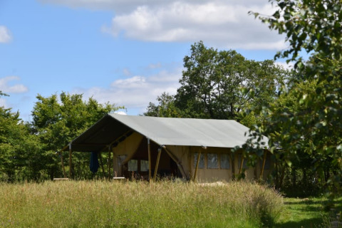 Safari tent at Camping Domaine Bleu Celeste in France, surrounded by lush trees and tall grass on a sunny day.