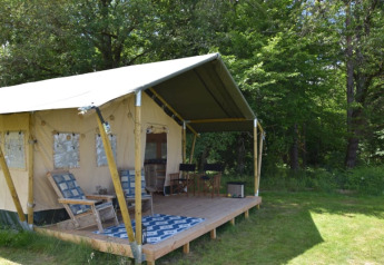 Tenda safari al Camping Domaine Bleu Celeste in Francia con veranda coperta e sedie immersa nel verde.