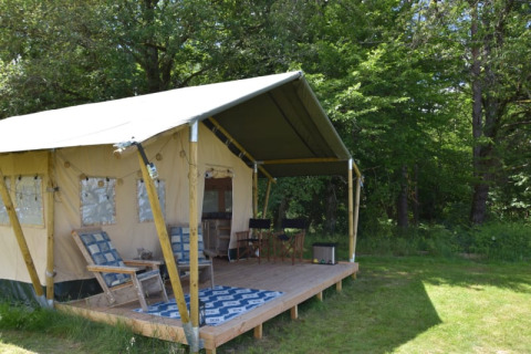 Tenda safari al Camping Domaine Bleu Celeste in Francia con veranda coperta e sedie immersa nel verde.