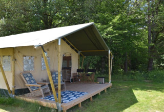 Tente safari au Camping Domaine Bleu Céleste en France, terrasse couverte et chaises dans un cadre verdoyant.