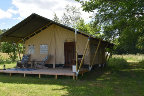 Safari-Zelt auf dem Camping Domaine Bleu Celeste in Frankreich mit Holzterrasse und Gartenstühlen.