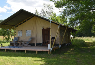 Safari-Zelt auf dem Camping Domaine Bleu Celeste in Frankreich mit Holzterrasse und Gartenstühlen.