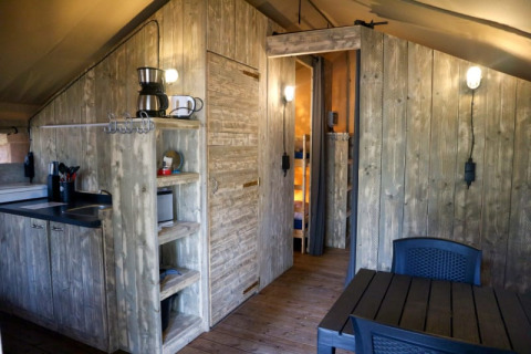 Vue intérieure d’une tente safari avec coin cuisine, table à manger, murs en bois et éclairage moderne.