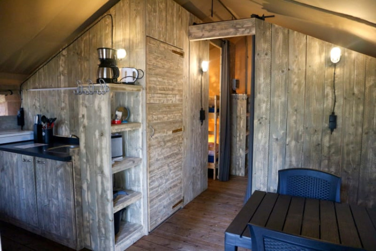 Interior view of a safari tent featuring a kitchenette, dining area, wooden walls, and modern lighting.