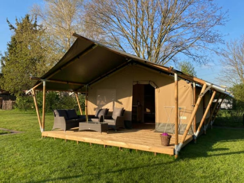 Tienda safari con terraza de madera, zona de asientos al aire libre y césped verde alrededor.
