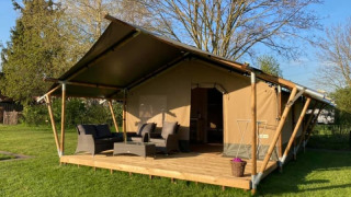 A safari tent with a wooden deck, outdoor seating area, and lush green grass surrounding the structure.