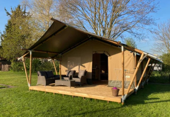 Tenda safari con veranda in legno, area salotto all'aperto e prato verde attorno alla struttura.