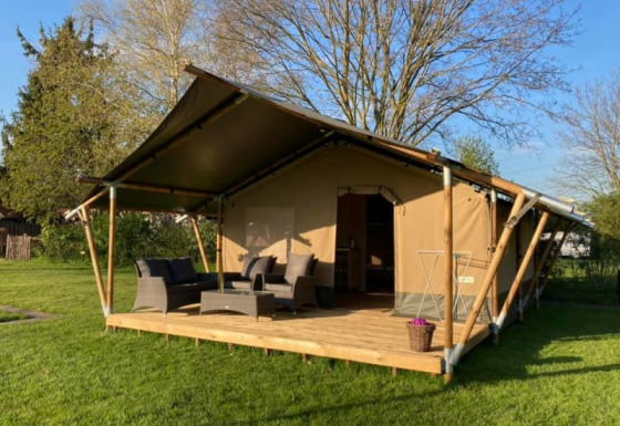 Tente safari avec terrasse en bois, coin salon extérieur et pelouse verdoyante sous le soleil.