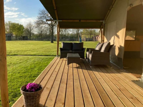 Terraza de madera con asientos de mimbre junto a una tienda safari en Camping de Peelweide, Países Bajos.