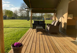Terraza de madera con asientos de mimbre junto a una tienda safari en Camping de Peelweide, Países Bajos.
