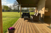 Terraza de madera con asientos de mimbre junto a una tienda safari en Camping de Peelweide, Países Bajos.