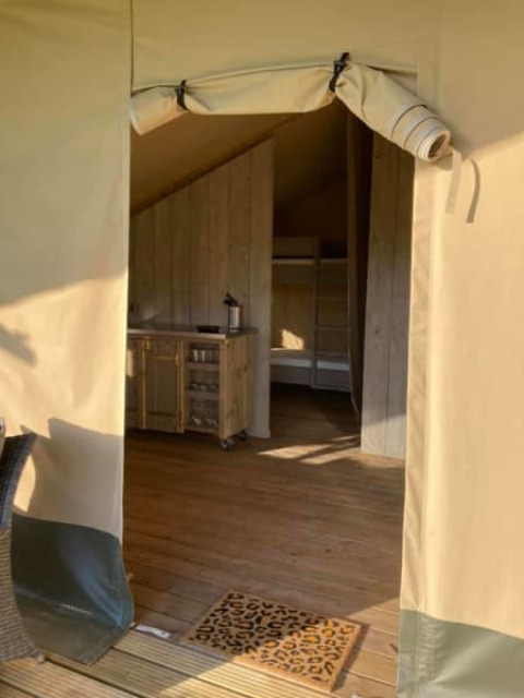 Entrada a una tienda safari en Camping de Peelweide, Países Bajos, con suelo de madera y cocina pequeña.