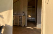 Entrada a una tienda safari en Camping de Peelweide, Países Bajos, con suelo de madera y cocina pequeña.