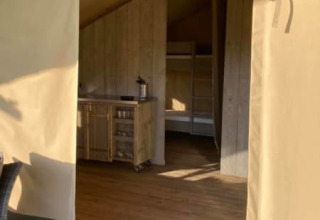 Entrada a una tienda safari en Camping de Peelweide, Países Bajos, con suelo de madera y cocina pequeña.