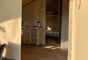 Entrada a una tienda safari en Camping de Peelweide, Países Bajos, con suelo de madera y cocina pequeña.