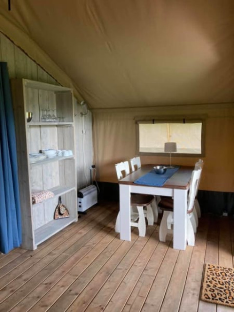 Vista interior de una tienda safari en Camping de Peelweide, Países Bajos, con mesa de comedor y estantería.