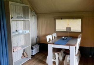 Vista interior de una tienda safari en Camping de Peelweide, Países Bajos, con mesa de comedor y estantería.