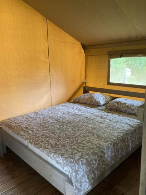 Vista interior de una tienda safari con cama doble en Camping de Peelweide, Países Bajos, durante el día.