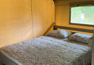 Vista interior de una tienda safari con cama doble en Camping de Peelweide, Países Bajos, durante el día.