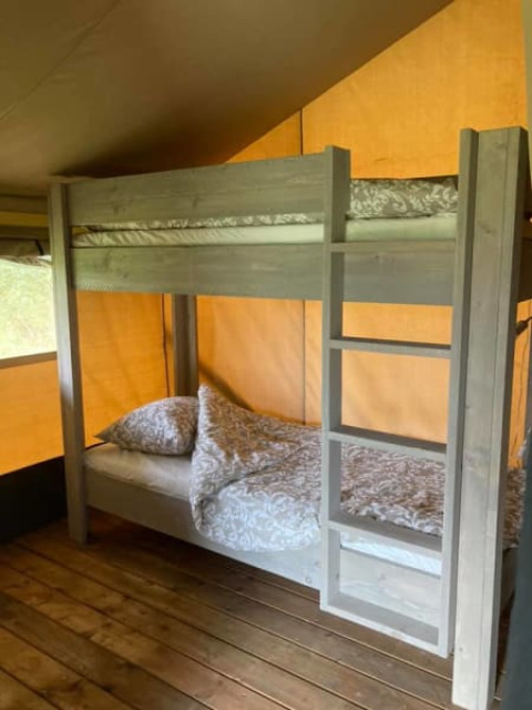 Køjeseng i en safaritelt med træbund og mønstrede dyner på Camping de Peelweide, Nederlandene.
