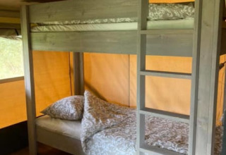 Litera en una tienda safari con suelo de madera y ropa de cama estampada en Camping de Peelweide, Países Bajos.