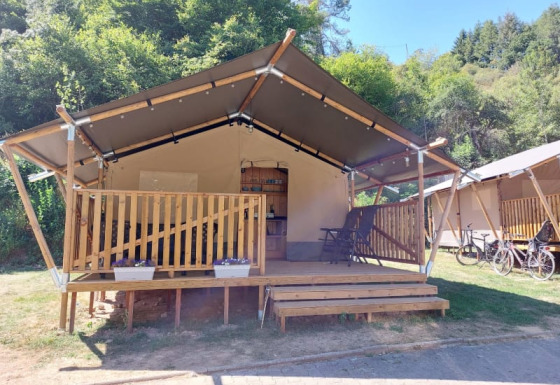 Tienda safari con porche de madera en entorno verde, bicicletas y cielo azul despejado de fondo.