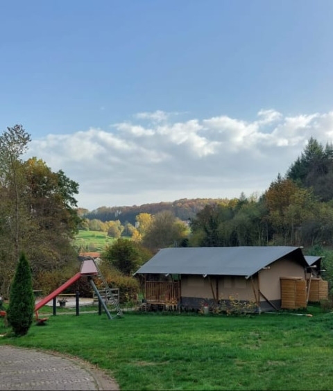 Safari tent with private sanitary at Camping Drei Spatzen, Germany, set in a green field with trees around.