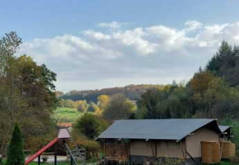 Safari tent with private sanitary at Camping Drei Spatzen, Germany, set in a green field with trees around.