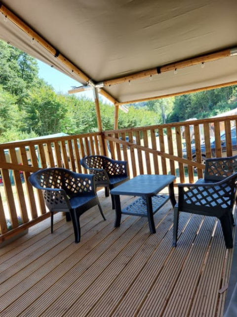Terraza cubierta con muebles de plástico en la tienda Safari + sanitario de Camping Drei Spatzen, Alemania.