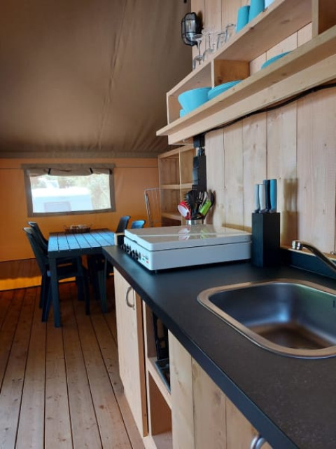 Kitchen space inside a safari tent with wooden shelves and dining table at Camping Drei Spatzen, Germany.