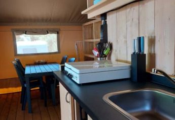 Área de cocina en tienda safari con estantes de madera y mesa comedor en Camping Drei Spatzen, Alemania.