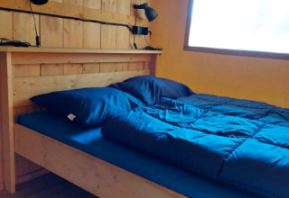 Vista interior de una cama de madera con ropa de cama azul y lámparas en una tienda safari, Camping Drei Spatzen.
