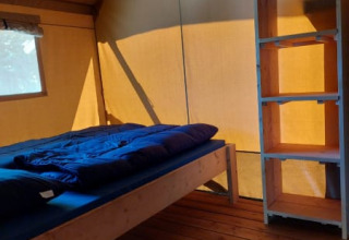 Indvendigt billede af et safari telt med en seng, trægulv og reol på Camping Drei Spatzen i Tyskland.