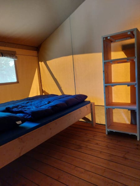 Vista interna di una tenda safari con letto, pavimento in legno e scaffale al Camping Drei Spatzen in Germania.