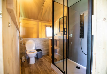 Moderne badkamer in een safaritent met toilet, douchecabine, wastafel en houten afwerking, goed verlicht.