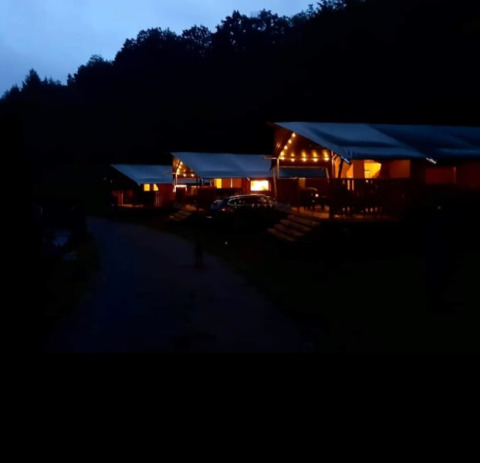 Evening photo of a safari tent with sanitary facilities at Camping Drei Spatzen in Germany, warmly lit up.