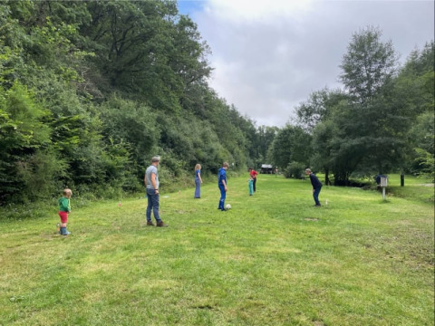 Familie spielt auf einer Wiese beim Safarizelt auf Camping Drei Spatzen in Deutschland, von Bäumen umgeben.