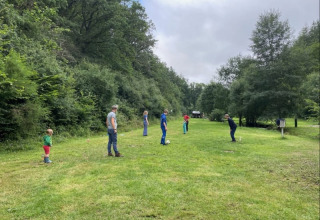 Familie speelt op een grasveld bij de safaritent op Camping Drei Spatzen in Duitsland, omgeven door bomen.