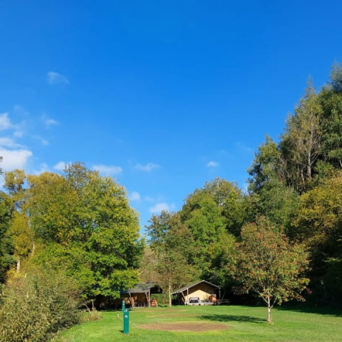Safari tent at Camping Drei Spatzen in Germany, surrounded by green trees and under a clear blue sky.