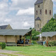 Safarizelt auf Campingplatz mit Steinkirche im Hintergrund und grüner Umgebung unter bewölktem Himmel.