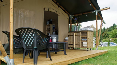 Safari tent at Camping La Dolce Vita in the Netherlands with wooden deck, plastic chairs, and an outdoor kitchen.
