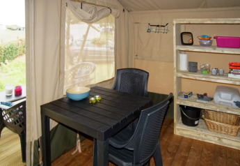 Vista interior de tienda safari en Camping La Dolce Vita, Países Bajos, con mesa, sillas y estantería.
