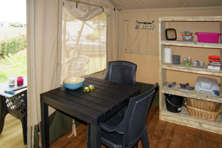 Vista interior de tienda safari en Camping La Dolce Vita, Países Bajos, con mesa, sillas y estantería.