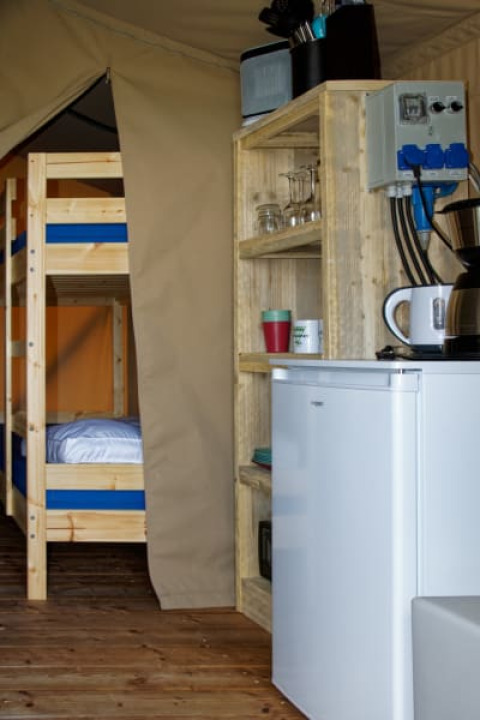 Interior de una tienda safari en Camping La Dolce Vita en los Países Bajos con literas y cocina pequeña.