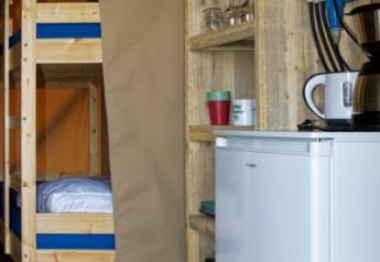 Interior de una tienda safari en Camping La Dolce Vita en los Países Bajos con literas y cocina pequeña.