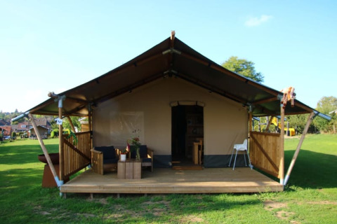 Safari-Zelt mit Sanitärbereich, Holzveranda, Sitzgelegenheiten draußen und viel grünem Rasen.
