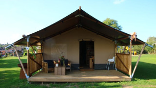 Tienda safari con sanitarios, terraza de madera, zona de estar al aire libre y césped amplio alrededor.